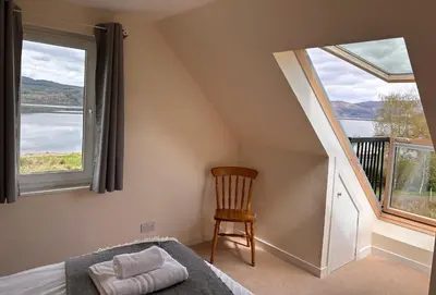 a bedroom with a bed and two windows and a chair at The Cottage, overlooking Loch Fyne in Cairndow