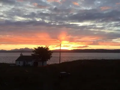 a sunset with a house next to the water at Archie's Cottage in Auchnacraig
