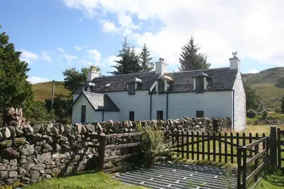 an old house with a stone wall and a fence at Barrachandroman Farmhouse in Lochbuie