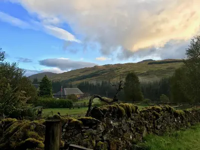 a stone fence in a field with hills in the background at Ewich House B&B in Crianlarich