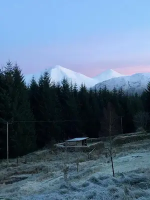 a house in a field with mountains in the background at Ewich House B&B in Crianlarich
