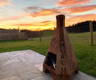 a wooden bottle with a fireplace in a backyard at Argaty Cottage in Doune