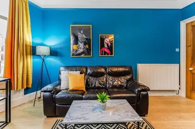 a living room with a leather couch and a blue wall at Traditional 1-Bed Flat in Southside (Hampden/Shawlands) in Glasgow