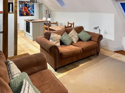 a living room with two brown couches and a kitchen at Craigdarroch Cottage in Saint Fillans