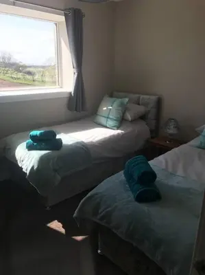 two beds in a room with a window at Inishroel Cottage in Campbeltown