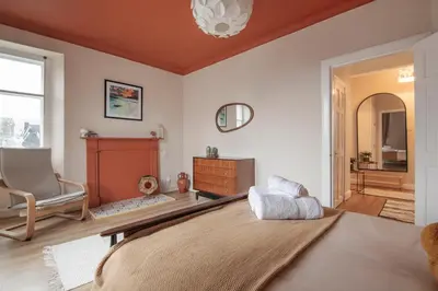 a bedroom with a bed and a chair and a mirror at Trendy 2 Bed Flat - Near Airport in Broxburn