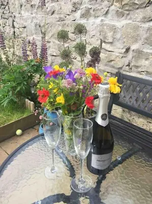 a bottle of wine and two glasses on a table with flowers at Wardie Garden Cottage in Edinburgh