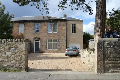 a man sitting on a wall in front of a house at Wardie Garden Cottage in Edinburgh
