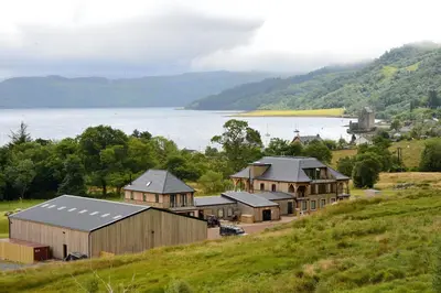 a group of buildings on a hill next to a body of water at The Lodge at Carrick Castle Estate in Cairndow