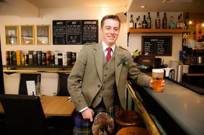 a man standing at a bar with a glass of beer at The Pipers' Tryst Hotel in Glasgow