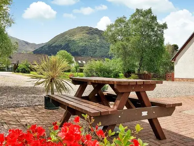 a wooden picnic table in a garden with flowers at Roe Deer Cottage in North Ballachulish