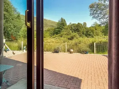 a door open to a brick courtyard with a fence at Roe Deer Cottage in North Ballachulish