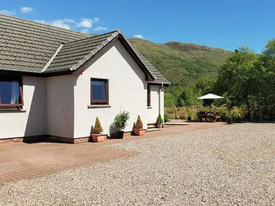 a white house with potted plants and a picnic table at Roe Deer Cottage in North Ballachulish