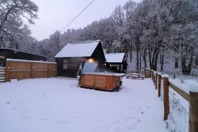 a cabin with snow on the ground next to a fence at 2 bed lodge with private hot tub in Aviemore in Saint Ninians