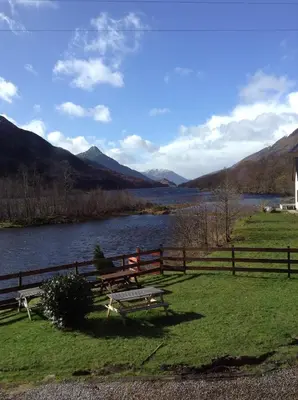 a bench sitting next to a fence next to a river at MacDonald Hotel & Cabins in Kinlochleven