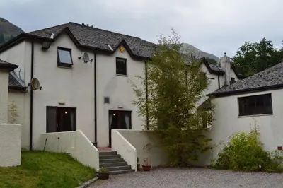 a white house with a staircase in front of it at MacDonald Hotel & Cabins in Kinlochleven