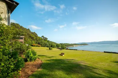 a park with a bench in the grass next to the water at Loch View House in Kilfinan