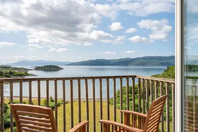 a balcony with two chairs and a view of a lake at Seal Bay Cottage in Kilfinan