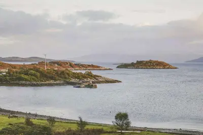 an island in the water with a boat in it at Seal Bay Cottage in Kilfinan
