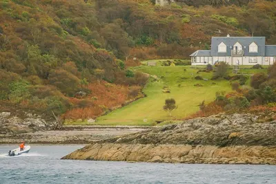 a boat in the water with a house in the background at Seal Bay Cottage in Kilfinan