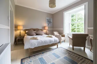 a bedroom with a bed and a chair and a window at Kilmaronock Manse B&B in Drymen