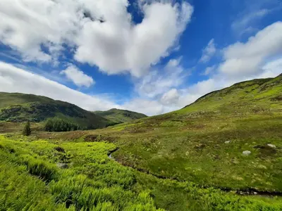a green grassy hill with a blue sky and clouds at Lochelour Mill Cottage in Perth