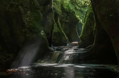 a waterfall in a cave in a forest at The Mar Huts - The Conic Hut in Drymen