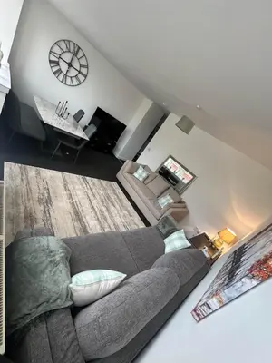 a living room with a gray couch and a clock at The M Rooms at 144 in Kirk of Shotts