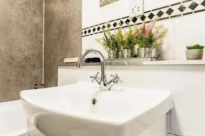 a white sink in a bathroom with flowers on a shelf at Spacious 2-Bedroom Main Door Apartment With Private Parking in Glasgow