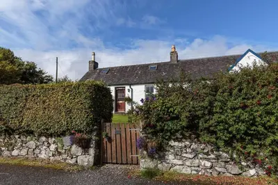 a white house with a stone fence and flowers at Seaview Cottage in Isle of Jura