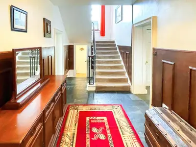 a hallway with a staircase and a red rug at Colzium Farmhouse in Blitterlees