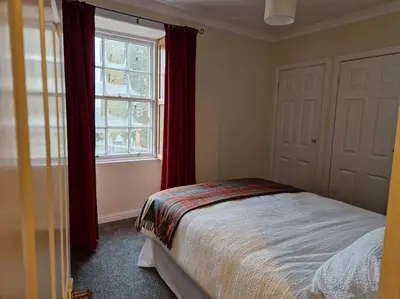 a bedroom with a bed with red curtains and a window at The Old Post Office House in Perth
