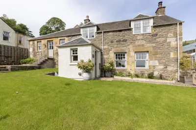 a stone house with a green lawn in front of it at Shepherds Cottage, Pentland Hills in Nine Mile Burn