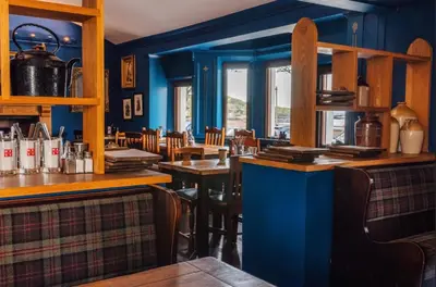 a restaurant with blue walls and wooden tables and chairs at Port Nan Gael Pods in Pennyghael