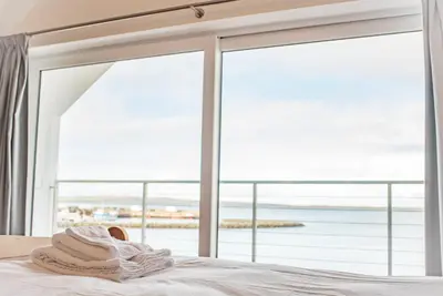 a stack of towels sitting on a bed in front of a window at The Saddlers House - best price per bed in Bowmore