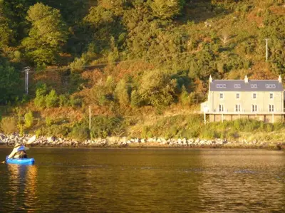 a person in a blue boat in the water with a house at Tigh na Breac - Great Outdoor Activity Location Oban in Bonawe
