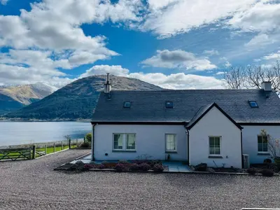 a house in front of a lake and mountains at Avoca Lodge in Fort William
