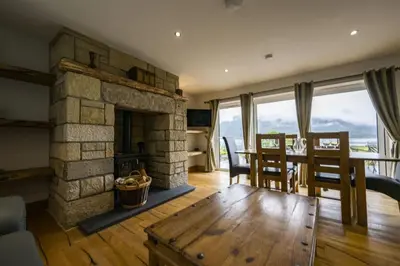 a living room with a stone fireplace and a table and chairs at Avoca Lodge in Fort William