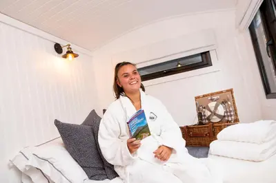 a woman sitting on a bed holding a book at The Mar Huts - The Lomond Hut in Drymen