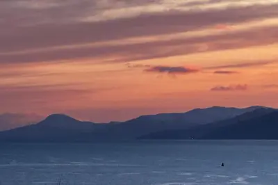a sunset over the ocean with mountains in the background at 1 Bedroom Cabin with Mountain & Loch Views - Quiet Location between Glencoe & Ben Nevis in Corran