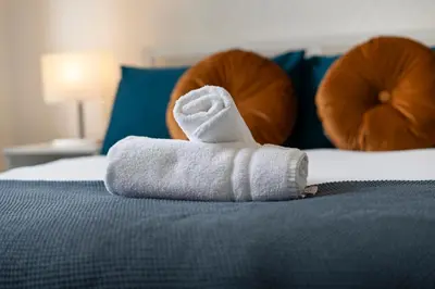 a white towel sitting on top of a bed at Free Parking - 2 Bedroom Flat-by Holiday Homes in Cambusnethan