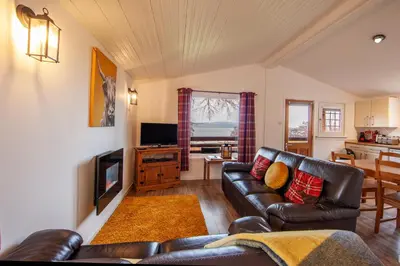 a living room with a leather couch and a television at Appin Holiday Homes -Caravans, Lodges, Shepherds Hut and Train Carriage stays in Appin