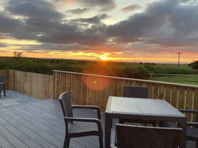 a deck with a table and chairs and a sunset at The Lodge at Blackhill Farm in Carluke