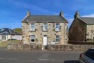 an old brick house with a white door on a street at Meadowfoot Haven in West Kilbride