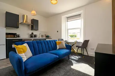 a blue couch in a living room with a kitchen at Meadowfoot Haven in West Kilbride