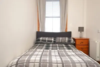 a bedroom with a bed with a plaid blanket and a window at Janeville Holiday Apartment in Ardrishaig