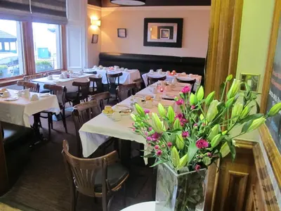 a dining room with white tables and flowers in a vase at The Spinnaker Hotel in Gourock