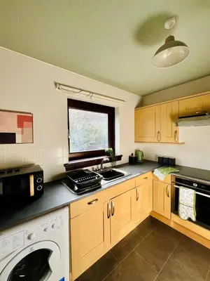 a kitchen with wooden cabinets and a washer and a window at Castle Gait Apartment in Paisley