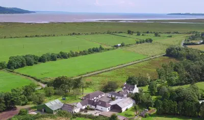 an aerial view of a house in a field and the ocean at Courtyard Cottages, Barn Cottage in Wigtown