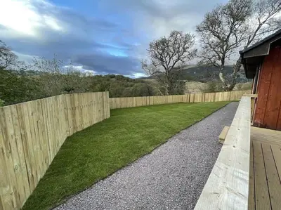 a backyard with a fence and a grass yard at Hot tub lodge with stunning view in Taynuilt